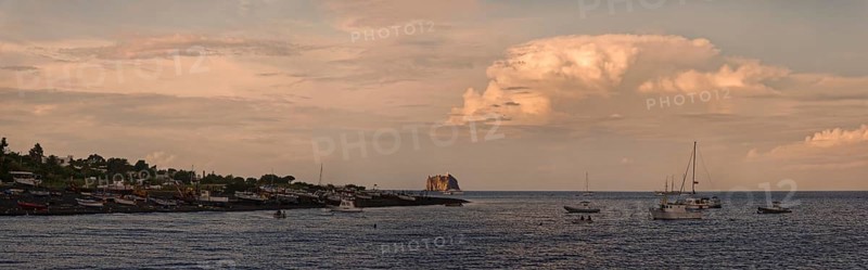 Small fishing village and harbour of San Vincenzo island and Stromboli volcano at sunset and anchored sailboats