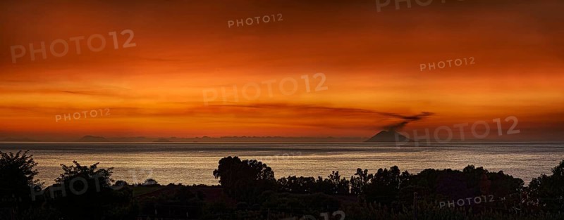 Strompoli volcano with plumes of smoke at sunset