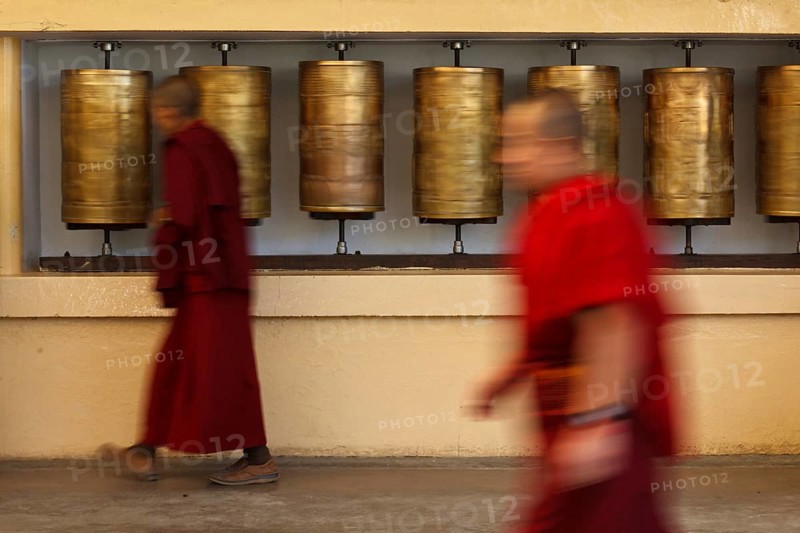 Buddhist monk passing and rotating prayer wheels on kora around Tsuglagkhang complex in McLeod Ganj