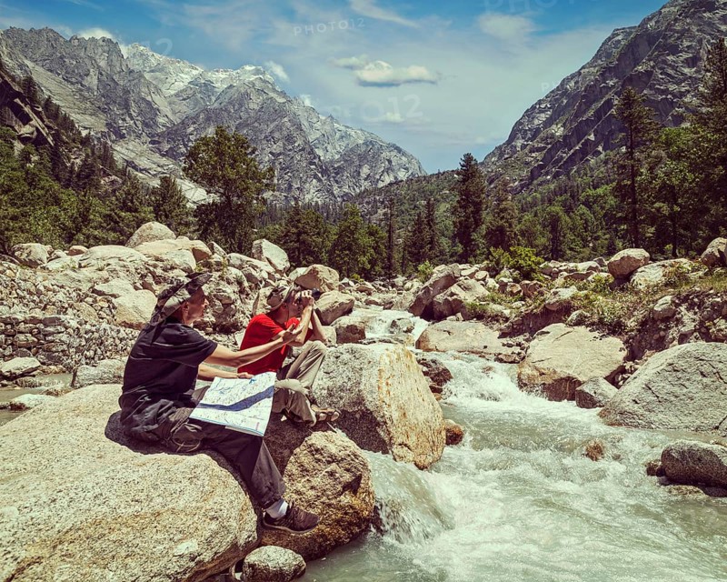 Vintage retro effect filtered hipster style image of hiker trekker tourists read a trekking map on trek in Himalayas mountains. Himachal Pradesh
