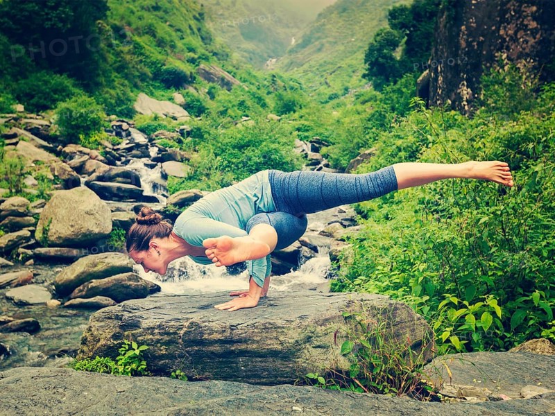 Vintage retro effect hipster style image of sporty fit woman doing yoga asana Eka Pada Koundinyasana 1 at tropical waterfall
