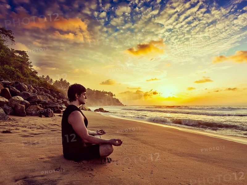 Vintage retro effect hipster style image of sporty fit man doing yoga meditating in padmasana lotus pose on tropical beach on sunset