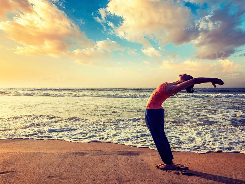 Vintage retro effect hipster style image of young sporty fit woman doing yoga Sun salutation Surya Namaskar pose Hasta Uttanasana on tropical beach on sunset