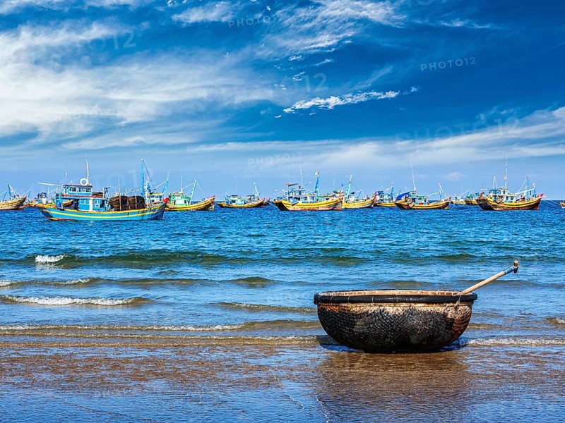 Coracle and fishing boats on beach in Mui Ne
