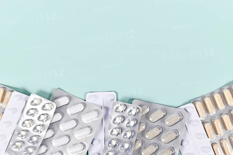 Blister packs with various pills and capsules at bottom of mint green background with copy space