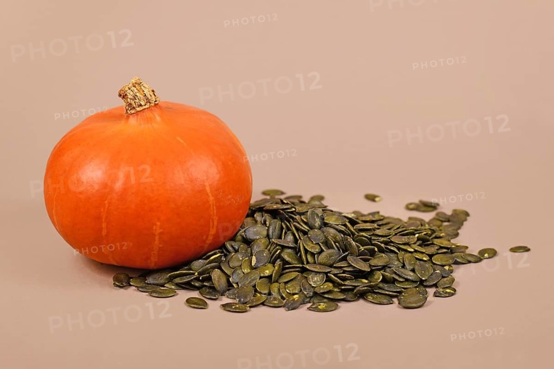 Green pumpkin seeds next to whole 'Red Kuri Hokkaido' squash