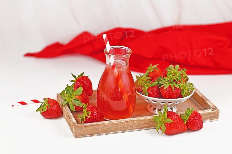 Strawberry fruit lemonade in jar surrounded by berries on wooden tray