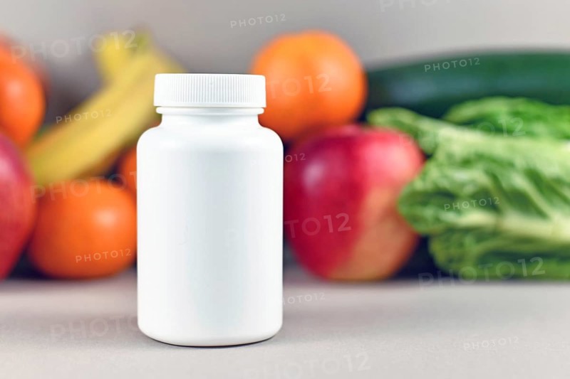Food nutrition supplement bottle in front of fruits and vegetables in blurry background