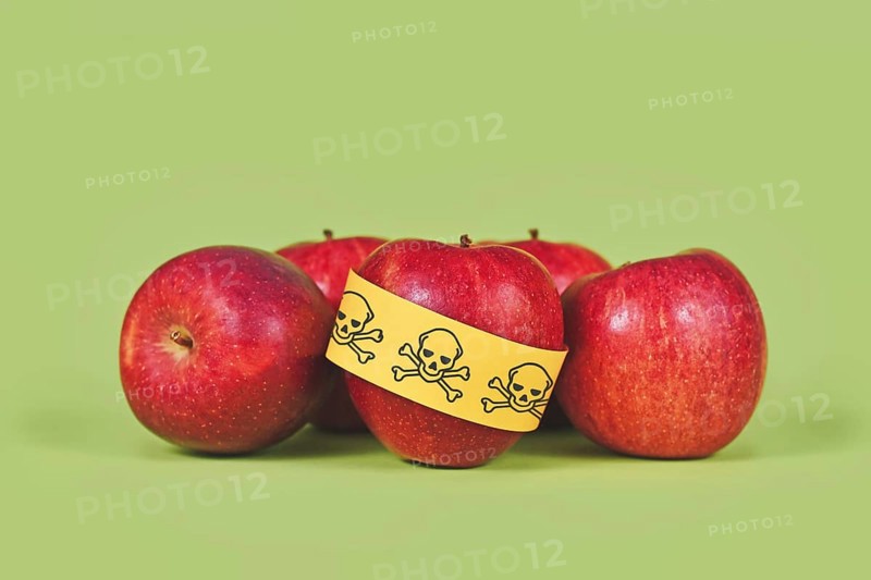 Apples with poison skull symbol sticker on green background. Concept of pesticide residues in agricultural food