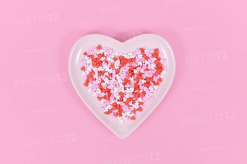 Plate with heart shaped sugar sprinkles on pink background