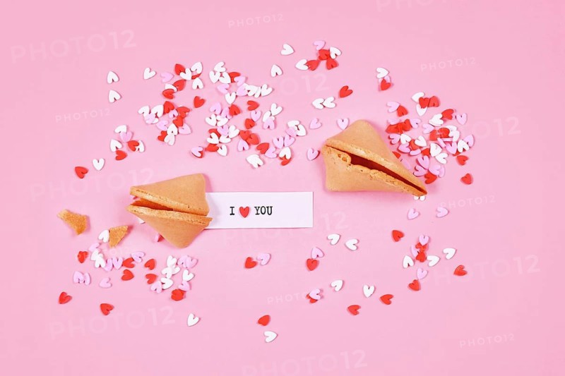 Fortune cookies with text 'I love you' and sugar sprinkle hearts on pink background