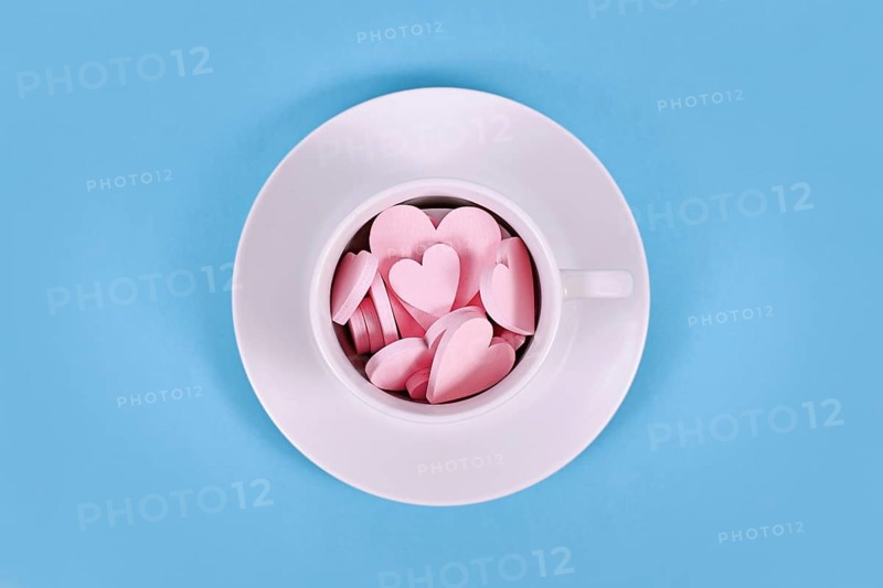 Pink wooden heart ornaments in white tea cup on blue background