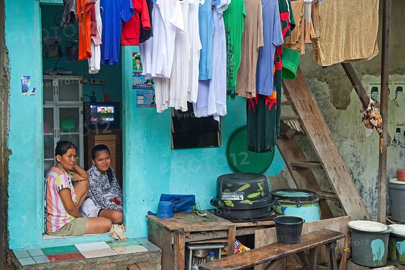 Indonesian mother and daughter at home with laundry drying on clothesline in Kota