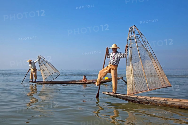 Two Intha fishermen steer traditional fishing boats by wrapping their leg around the oar