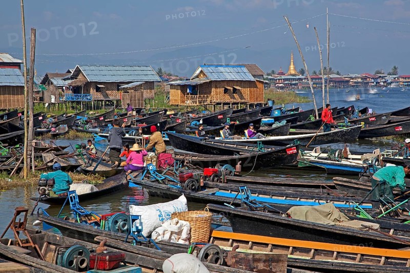 Open boats in lakeside village with traditional wooden houses on stilts in Inle Lake