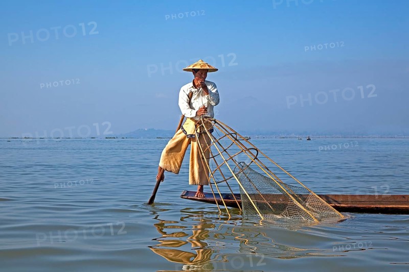 Intha fisherman steering traditional fishing boat by wrapping his leg around the oar