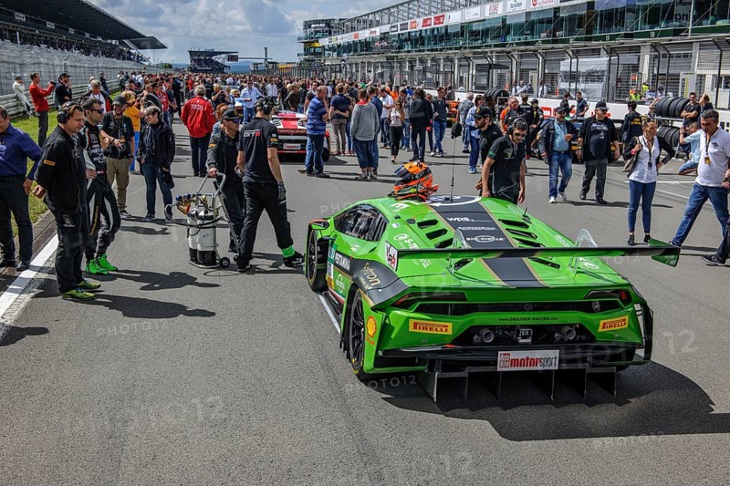 Motorsport fans audience of motor racing event inspects racing car Lamborghini Huracan GT3 on start-finish straight Gridlane of race track in front of start