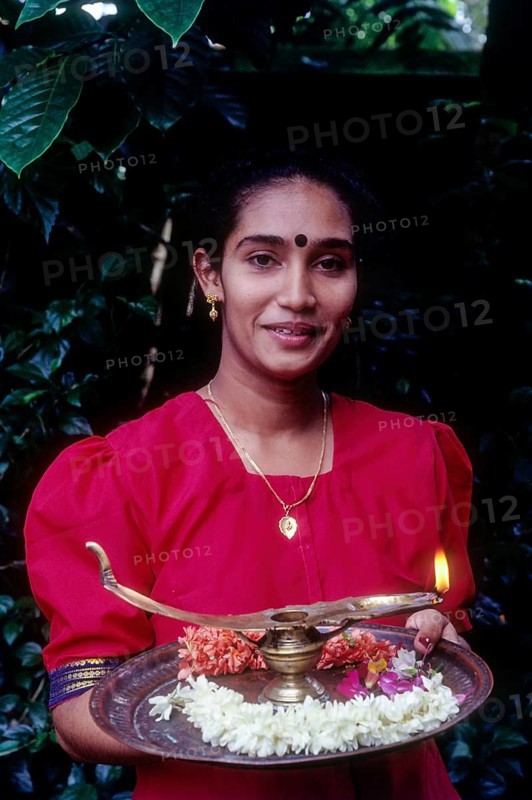A girl holding oil lamp and flowers on a tray during Onam festival