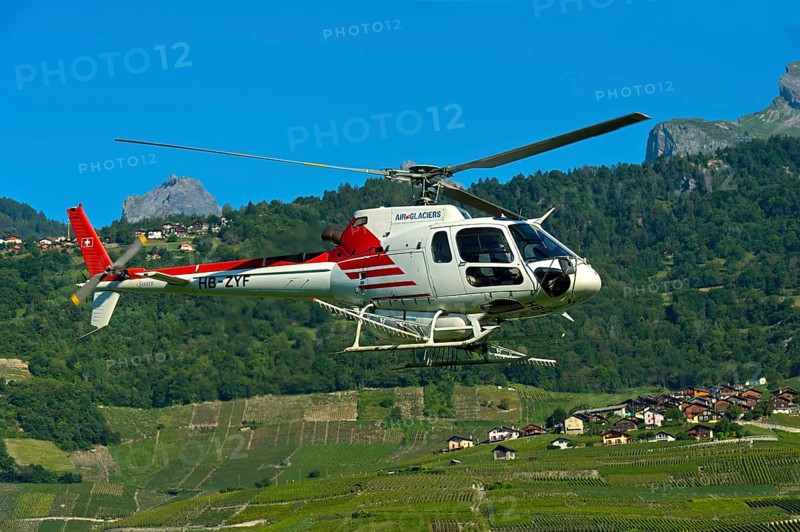 Helicopter Eurocopter AS350 B2 Ecureuil of Air-Glaciers SA flying over the wine growing area of Leytron at the foot of the Swiss Alps