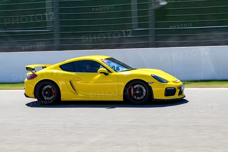 Yellow racing car sports car Porsche Cayman GT4 races at high speed top speed during trackday on start-finish straight of race track