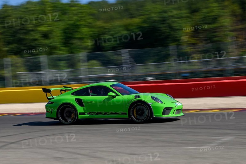 Green racing car sports car Porsche 911 GT3 RS races at high speed full throttle at exit of curve hairpin La Source of race track