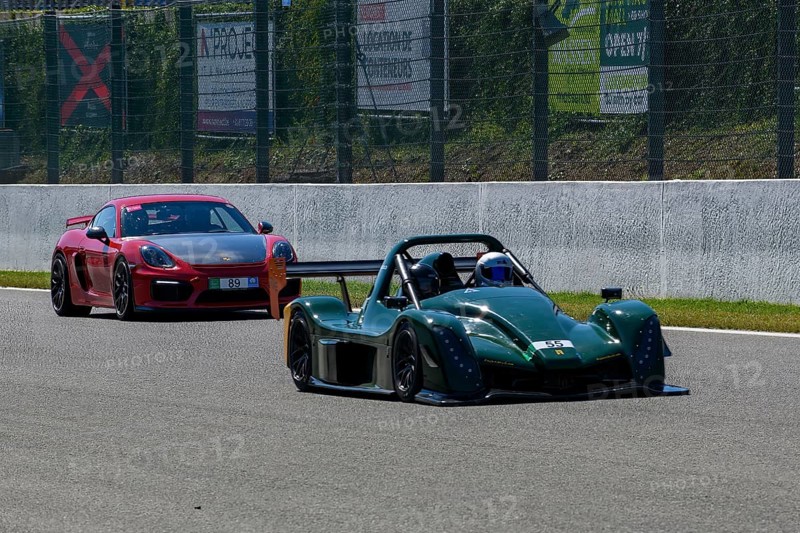 Radical SR10 open-wheel racing car in front behind Porsche Cayman GT4 races at high speed top speed during trackday on start-finish straight of race track