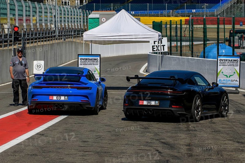 Two Porsche GT3 sports cars waiting at red lights at pit lane exit for clearance to enter race track