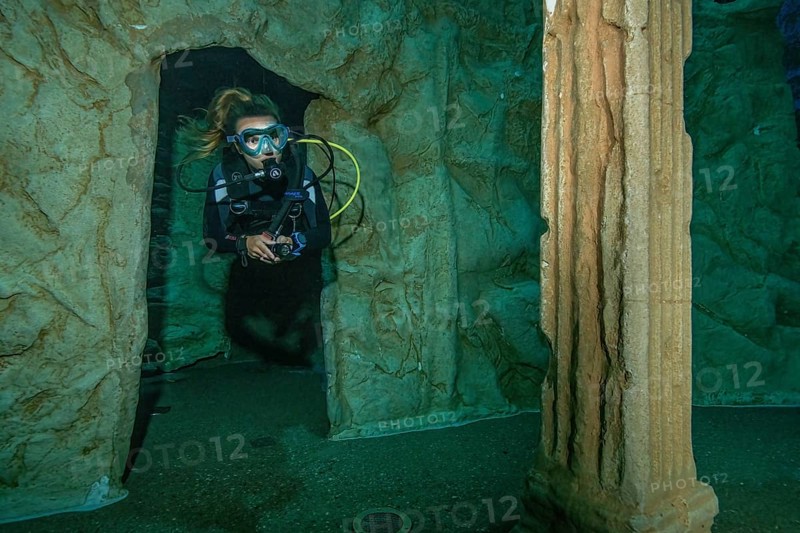 Diver dives through small gate of stylised ruin of ancient temple in 20 metres depth in indoor diving tower