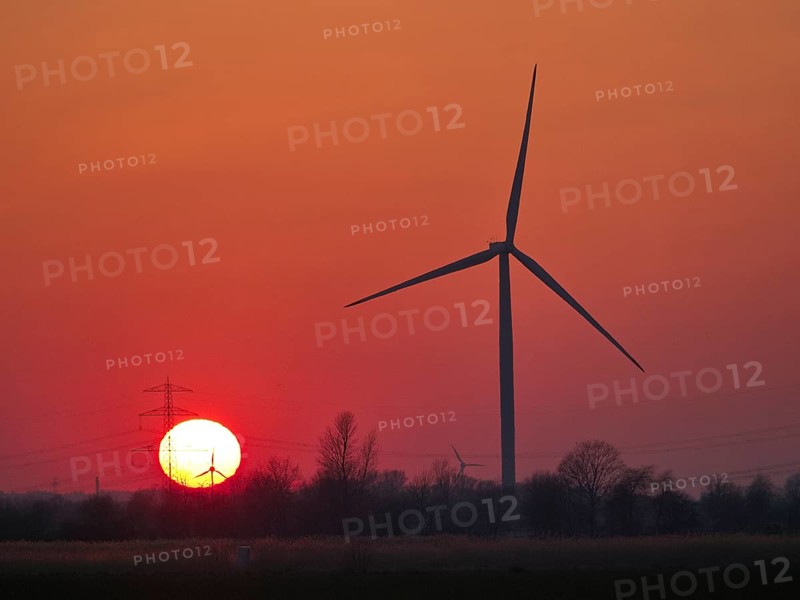 Wind turbines and power lines in front of the setting sun in Hamburg's Vier- und Marschlanden. Ochsenwerder