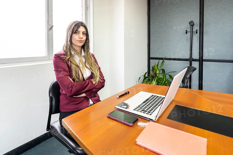Young blonde businesswoman sitting with her arms crossed at the head of the table in the office meeting room