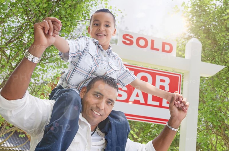 Happy young hispanic father and son in front of sold for sale real estate sign