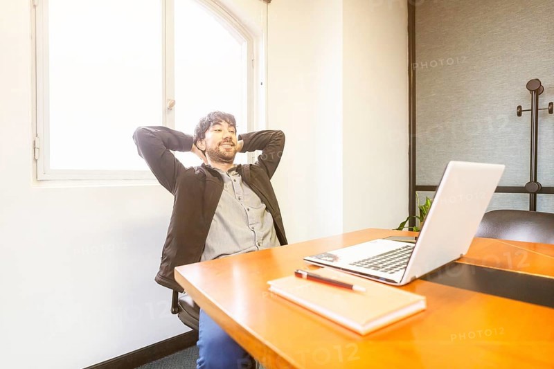 Businessman sitting at the head of the meeting table with his hands behind his head