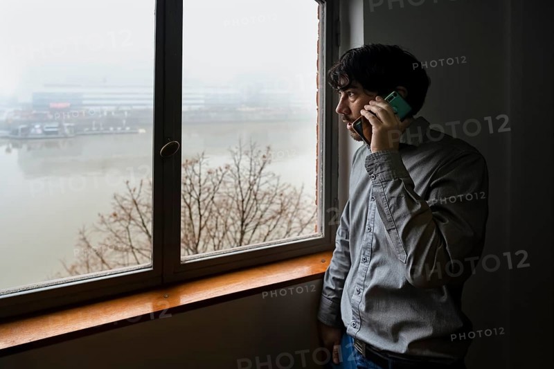 Latino businessman working in an office overlooking the river. Talking on the phone while he looks out the window