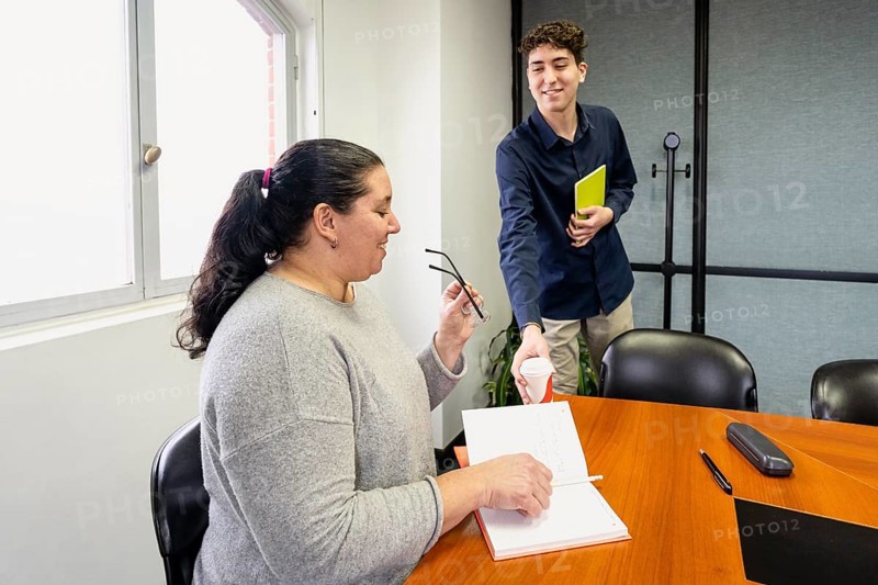 Assistant serving coffee to businesswoman sitting at head of meeting table