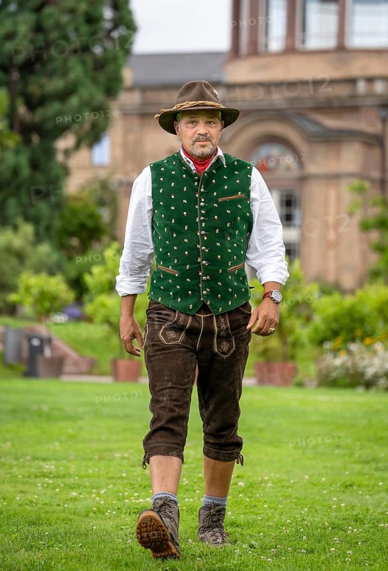 Man in Bavarian traditional costume with hat walking across lawn