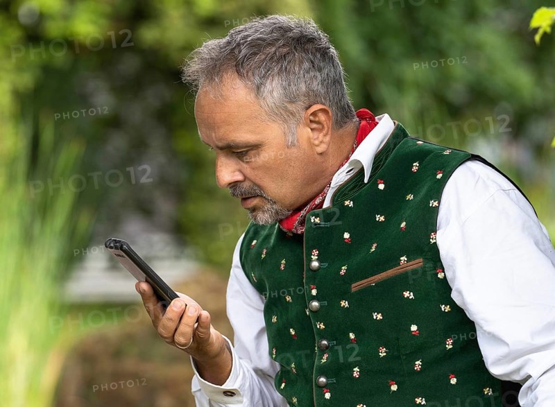 Middle-aged man in Bavarian traditional costume looking confused at his phone