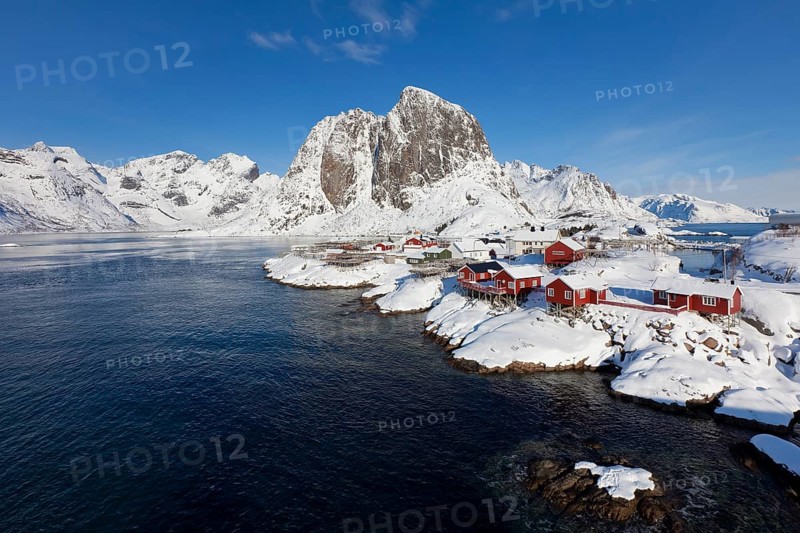 Rorbuer huts and wooden racks with stockfish to dry by Hamnoy fjord in the snow in winter