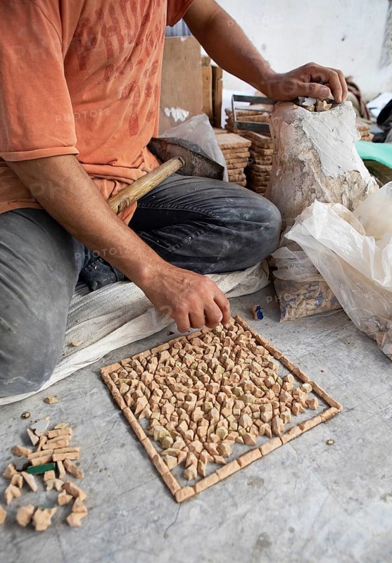 Moroccan cellular craftsman at work: hammering small pieces out of a tile