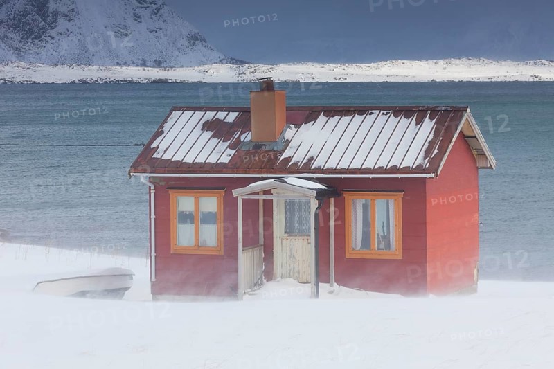 Red insulated wooden hut along the coast in the snow in winter