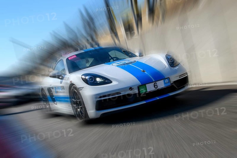 Dynamic photo with zoom effect of sports car racing car white with blue stripe Porsche 718 Cayman GTS leaving pit lane