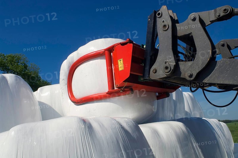 Plastic wrapped round silage bales stacked on a pile with mechanical loader