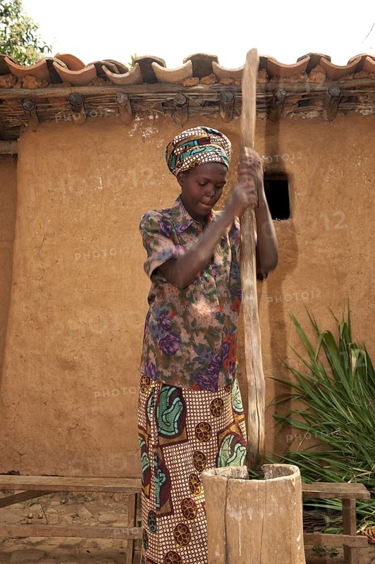 Woman beating cassava with a stick into a wooden pot to make flour