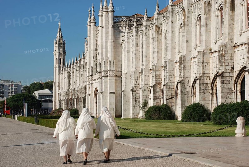 Three nuns walking outside late-Gothic Monastery