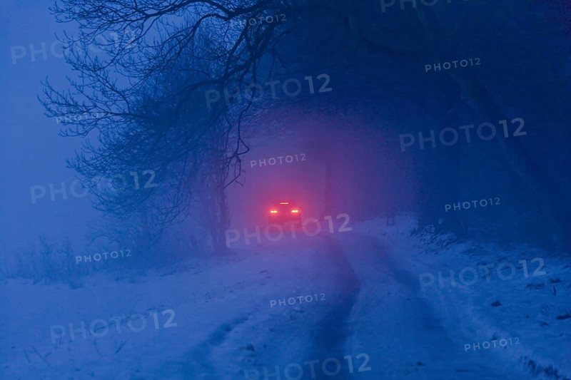 Distant brake lights of a car on a snow-covered road in freezing fog at dusk