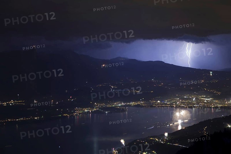 Thunderstorm with lightning and fireworks over town and lake at night