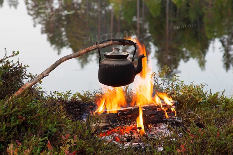 Blackened tin kettle boiling water over the flames of the campfire during a hike by the lake