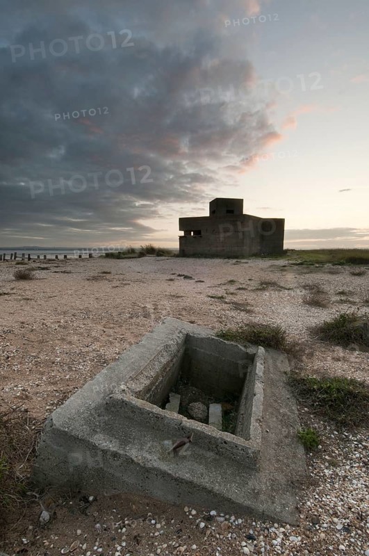 Remains of a World War II log cabin on a shingle beach at sunset