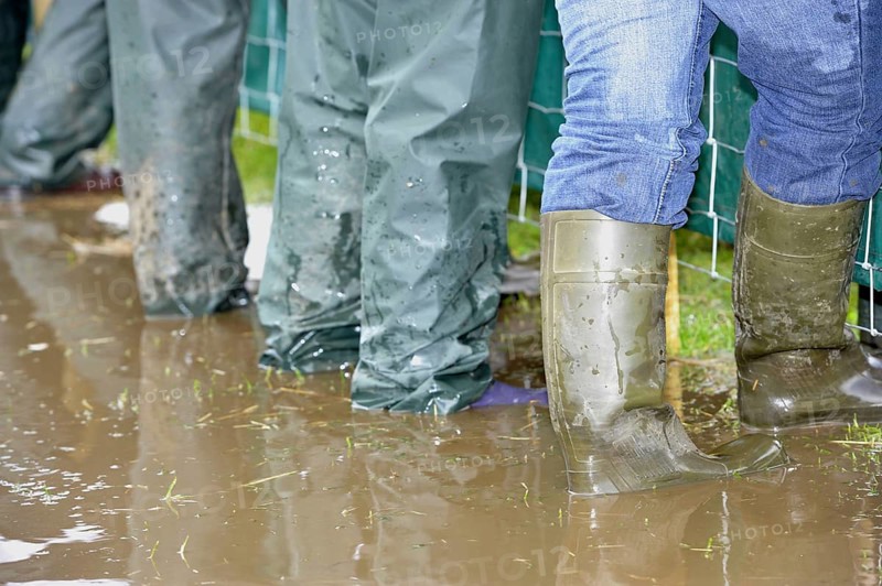 Farmers wearing wellington boots and waterproofs standing in puddle of muddy water
