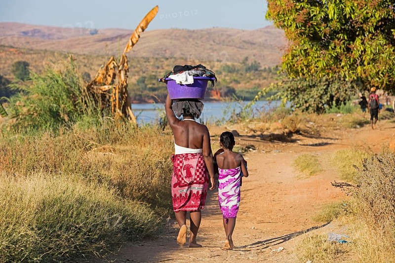 Malagasy daughter and mother carrying a laundry basket on their heads while walking along the Tsiribihina River