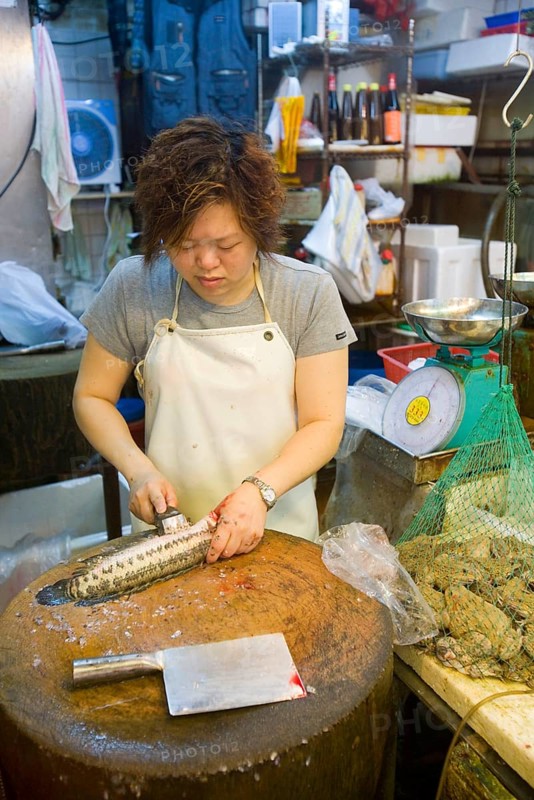 Woman preparing fish next to frogs in a net at the fish market